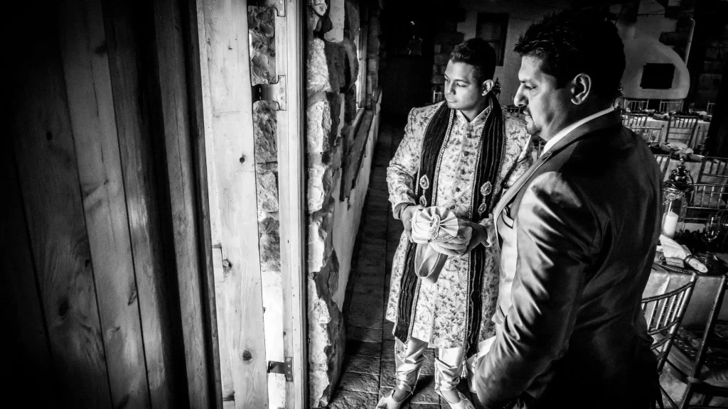 A black and white photo of a groom with his father looking out through a door.