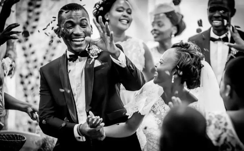 A black and white photo capturing a excited bride and groom in celebration while guests through confetti over them.