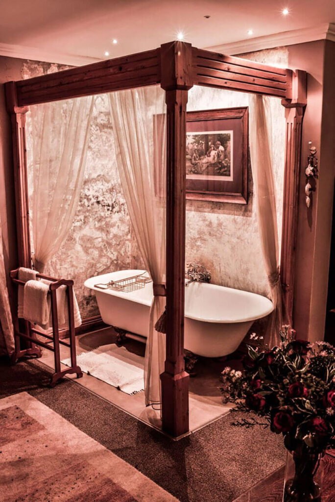 A antique ball and claw bathtub in a wooden four post frame with white curtains.