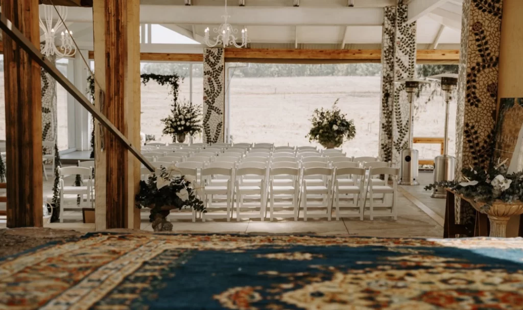 A wedding ceremony in a barn with chairs and a rug.
