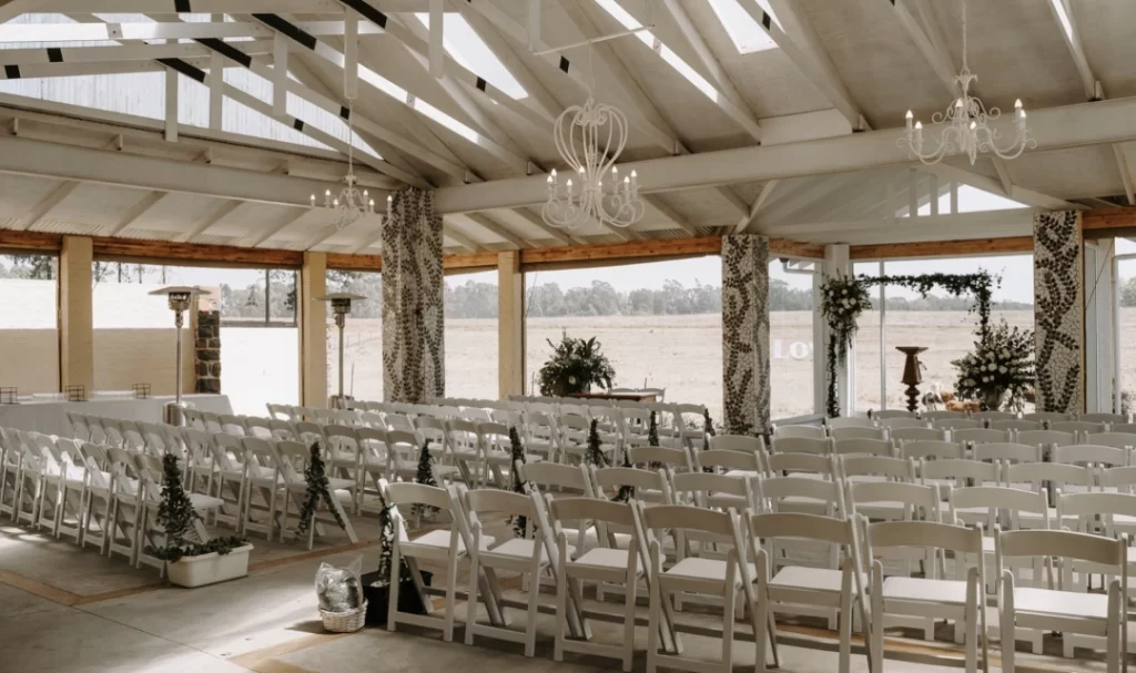 A wedding ceremony set up in a barn with white chairs.